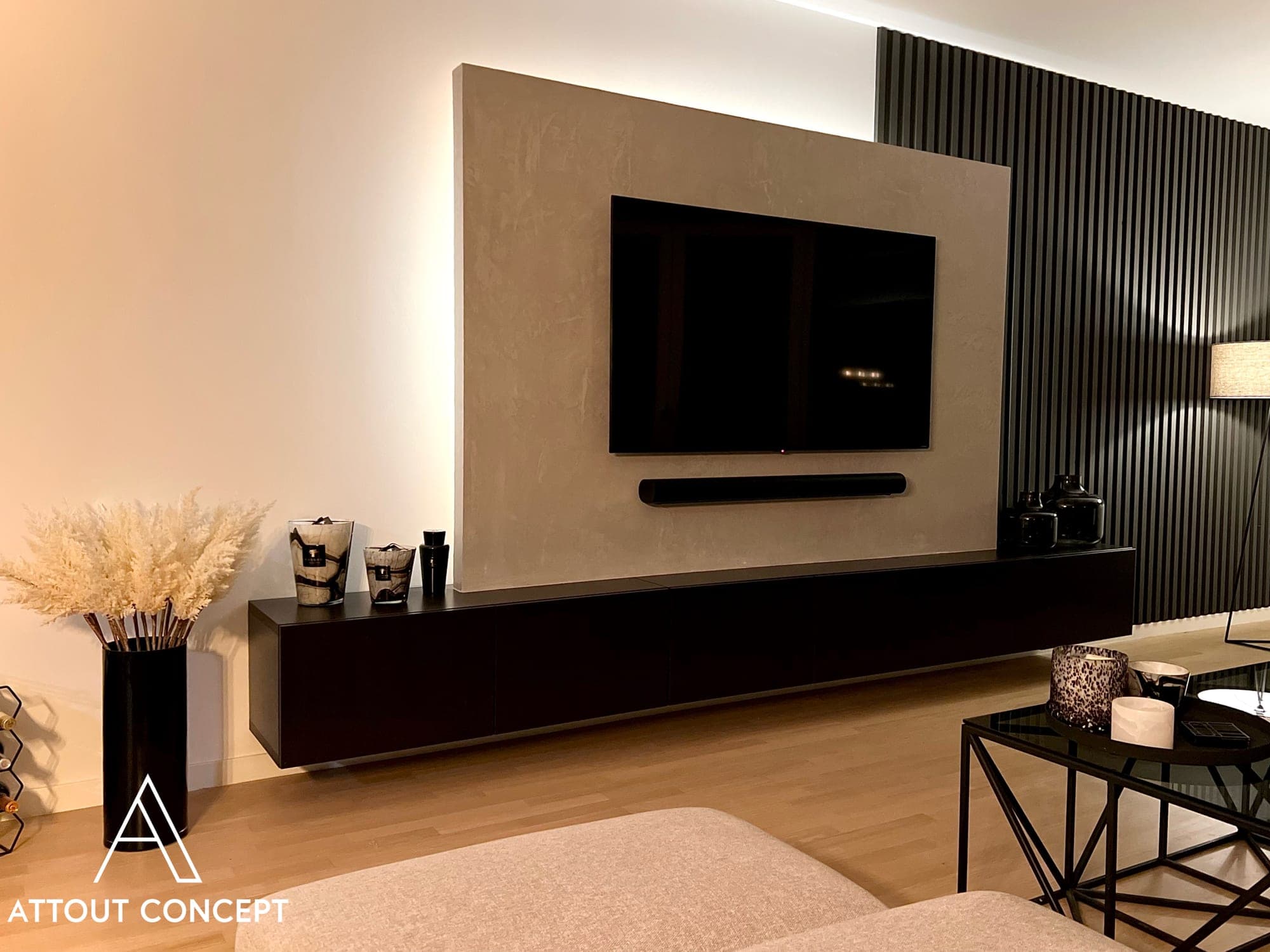 Panneau TV en enduit décoratif effet béton rétroéclairé, meuble bas noir et claustra en tasseaux